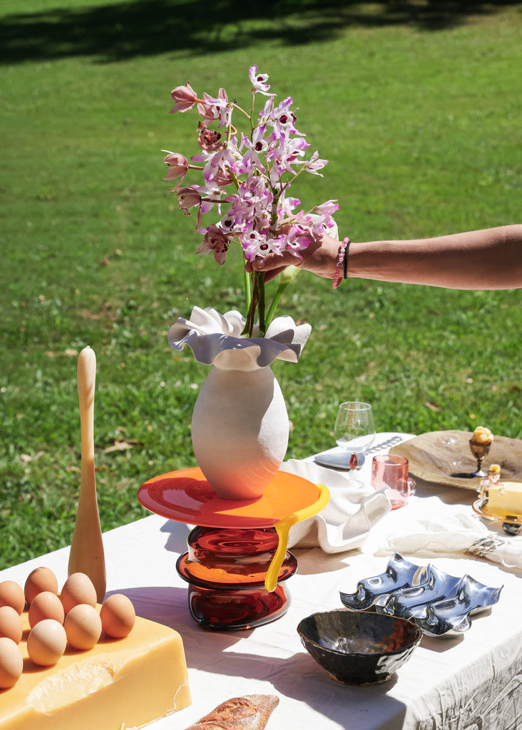 Hand putting flowers in vase ontop of platter on curated table
