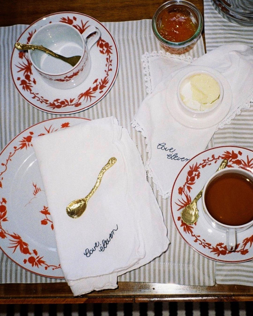 Eleven napkin with brass artisanal spoon on table with tea and matching plates 
